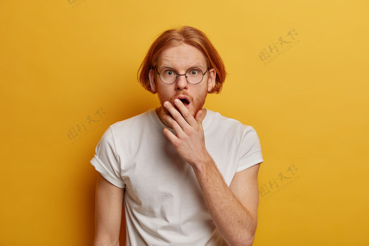 反应惊呆了的红发男人对季节性的折扣反应 目瞪口呆 捂着嘴 戴着眼镜和白t恤 孤立在黄色的墙上 忘了什么天哪眼镜青少年同伴