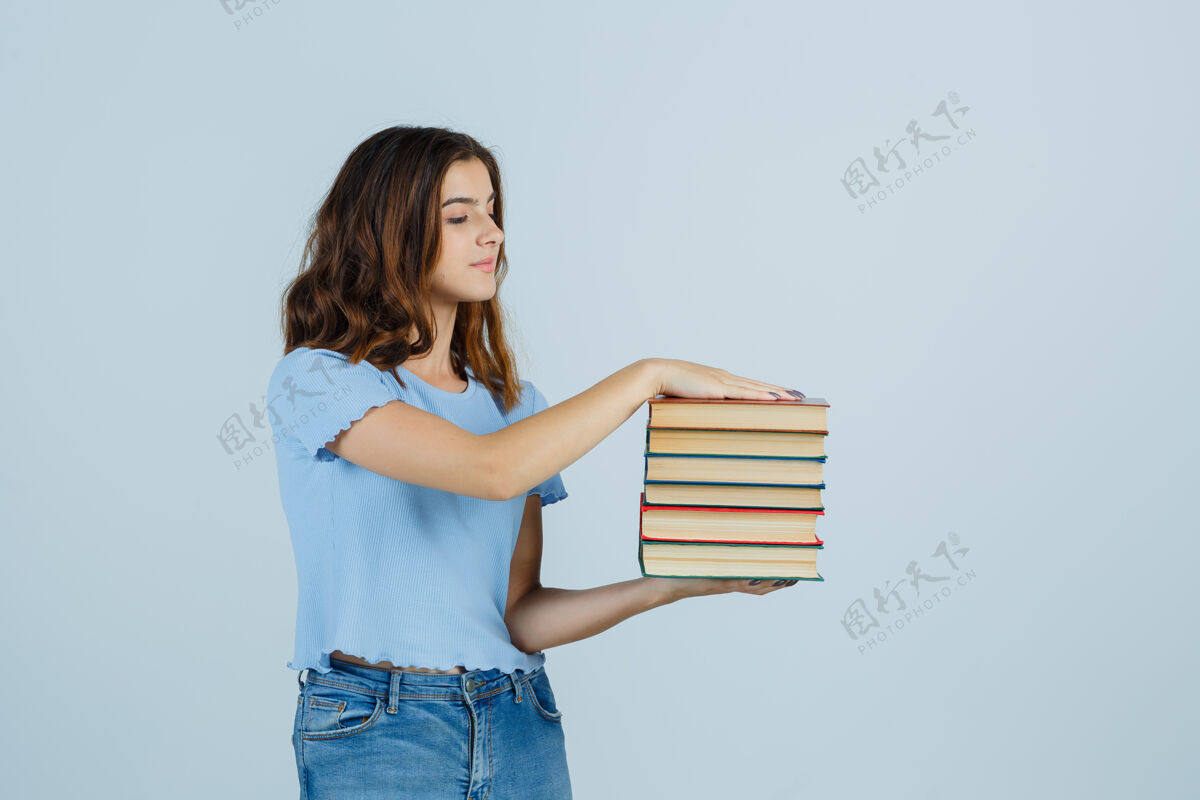 魅力年轻的女士拿着书 穿着t恤 牛仔裤 看上去很小心前视图肖像新鲜完美