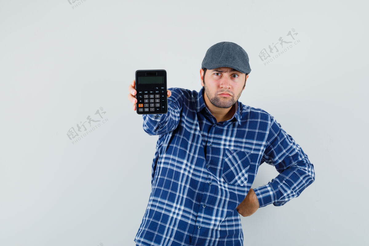 站一个穿着衬衫 戴着帽子的年轻人正在看计算器 他看上去很可疑 正对着窗外快乐男人聪明