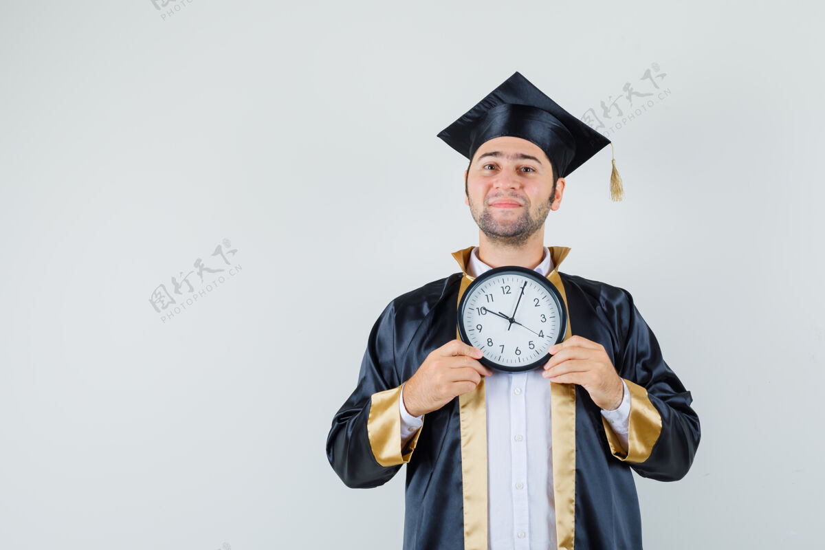 男年轻人拿着挂钟 穿着毕业制服 兴高采烈地看着墙模特聪明