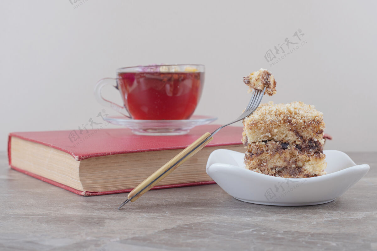烘焙一杯茶放在一本书上 旁边是一小块蛋糕放在大理石上甜点切片芳香