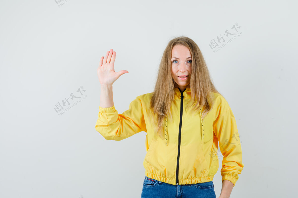女人身穿黄色棒球服和蓝色牛仔裤的年轻女子展示停车标志 表情严肃正视图年轻漂亮模特