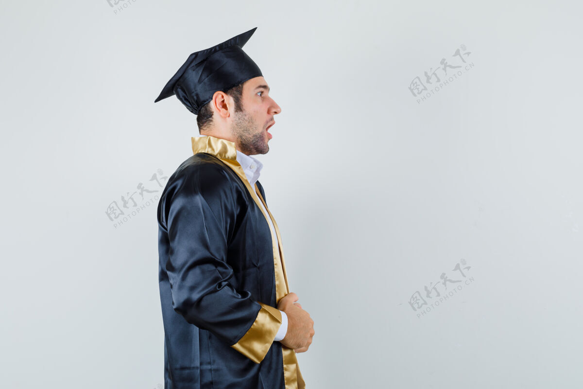 肖像年轻的男性拿着他的毕业礼服 看起来很惊讶模特男人男人