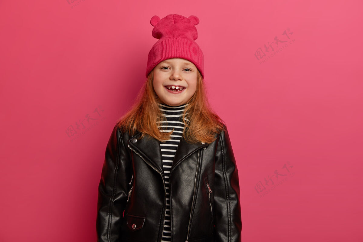 欧洲积极微笑的红头女孩积极地笑着 戴着粉红色的帽子和皮夹克 看起来很高兴 隔着粉红色的墙孩子们 时尚概念可爱的女儿喜欢购物搞笑小生姜
