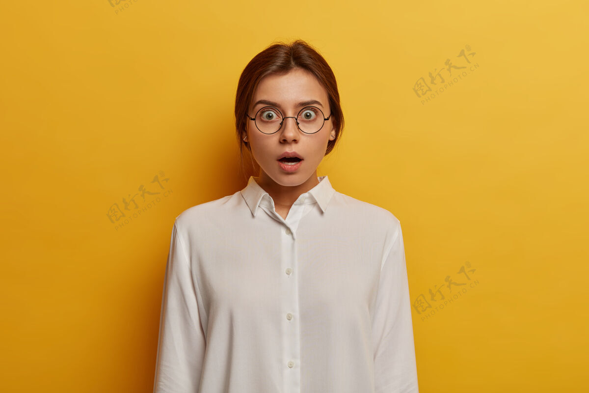 意外天哪 我不相信震惊情绪化的女人戴着大眼镜和白衬衫 对令人惊讶的消息做出反应 睁大眼睛 隔着黄色的墙人和情绪的概念干净情绪眼镜