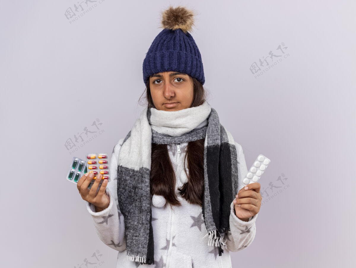 帽子未出狱的生病的年轻女孩戴着冬天的帽子 戴着围巾 拿着隔离在白色背景上的药丸药丸生病女孩