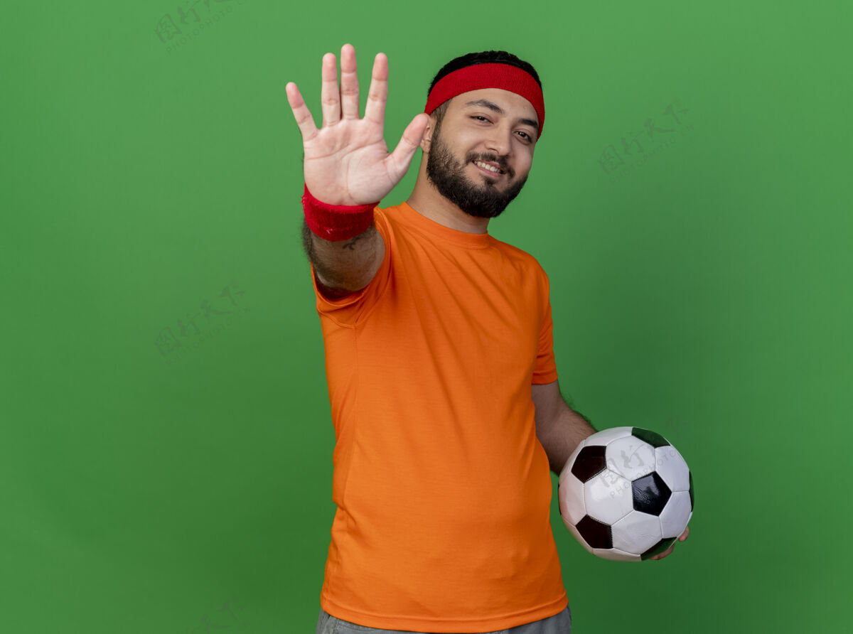 头带微笑的年轻运动男子戴着头带和手环拿着球在绿色背景上显示五个孤立的复制空间年轻球五