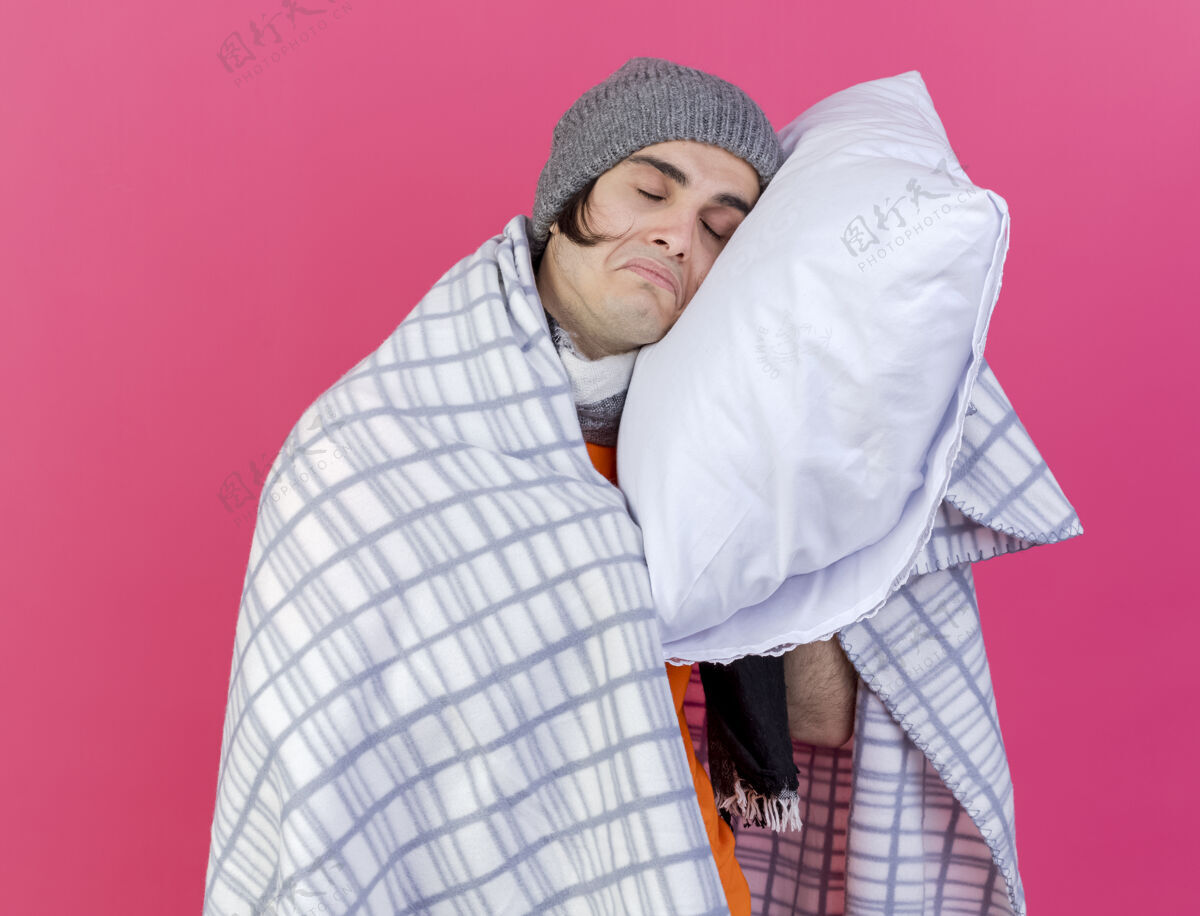 枕头闭上眼睛悲伤的年轻病人戴着冬天的帽子 用格子布裹着围巾 把头放在枕头上 隔离在粉红色的背景上包裹年轻封闭