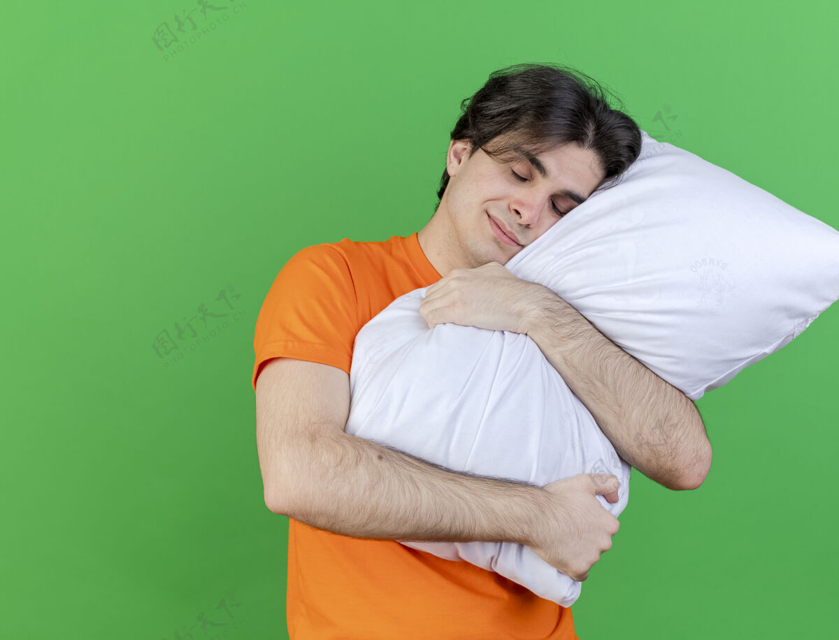 年轻年轻的病夫高兴地闭上眼睛 抱着一个被隔离在绿色背景上的枕头枕头拥抱眼睛