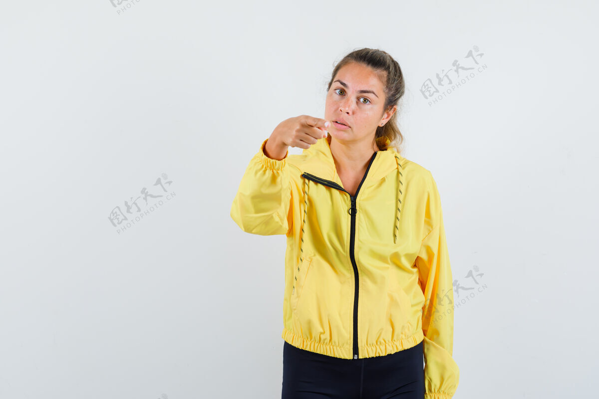漂亮金发女人用食指指着前面 穿着黄色棒球服和黑色裤子 看起来很漂亮干净肖像可爱