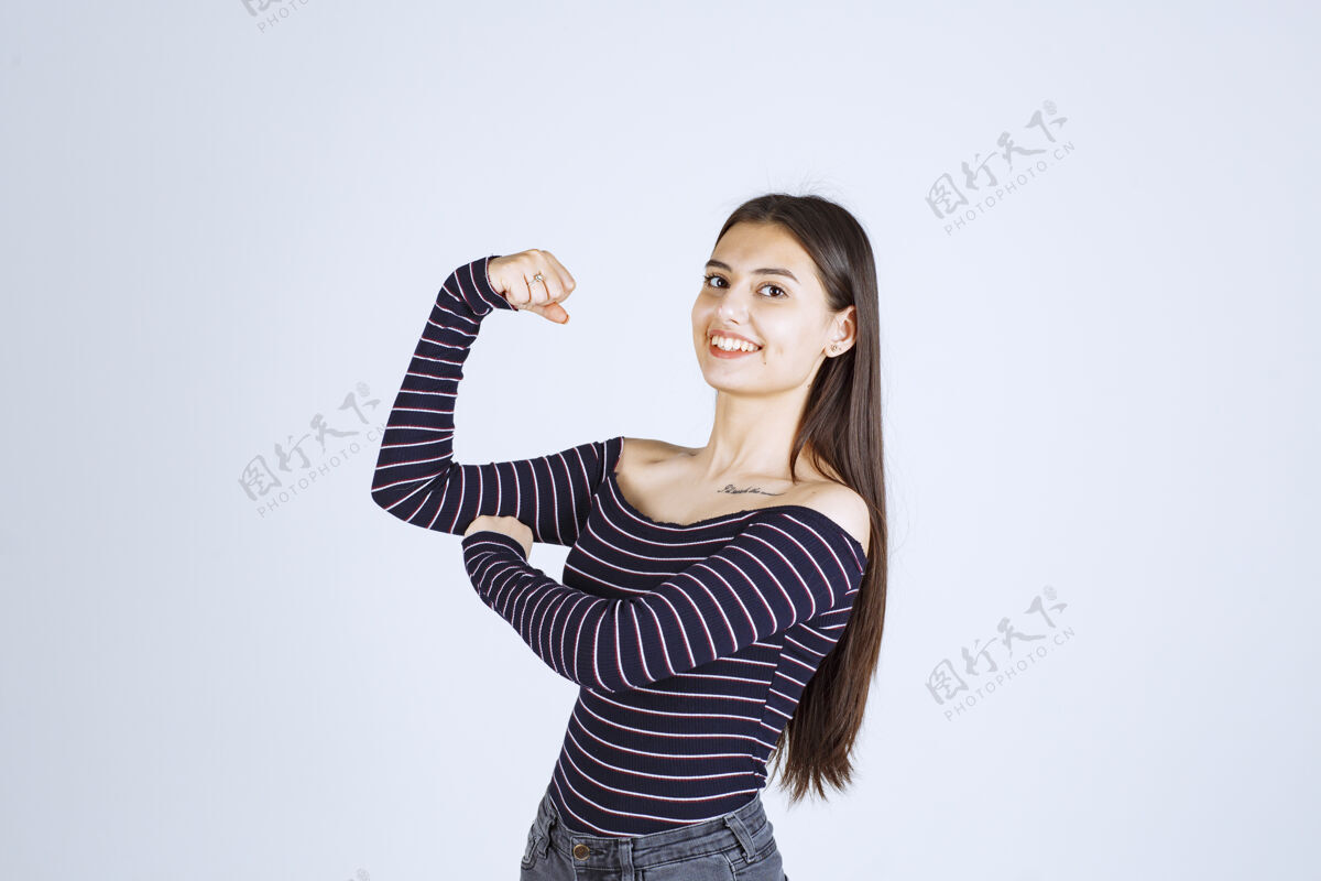 幸运穿条纹衬衫的女孩展示她的手臂肌肉成人休闲运动
