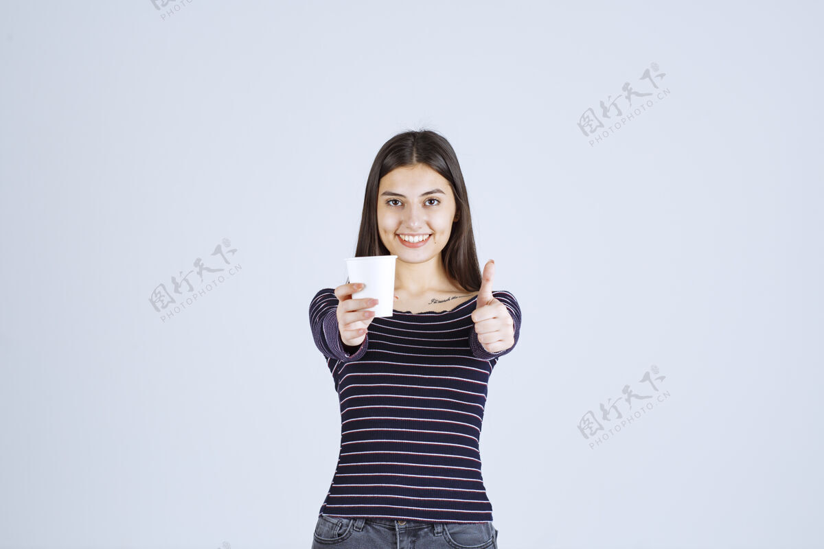 雇员穿着条纹衬衫的女孩拿着一个塑料咖啡杯 指着一个好味道人体模特成人人类