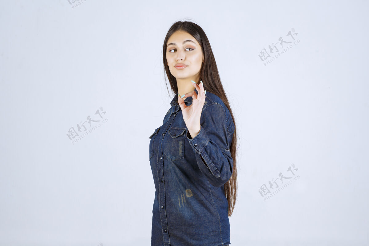 人穿着牛仔衬衫的年轻女子展示着享受的标志积极休闲模特