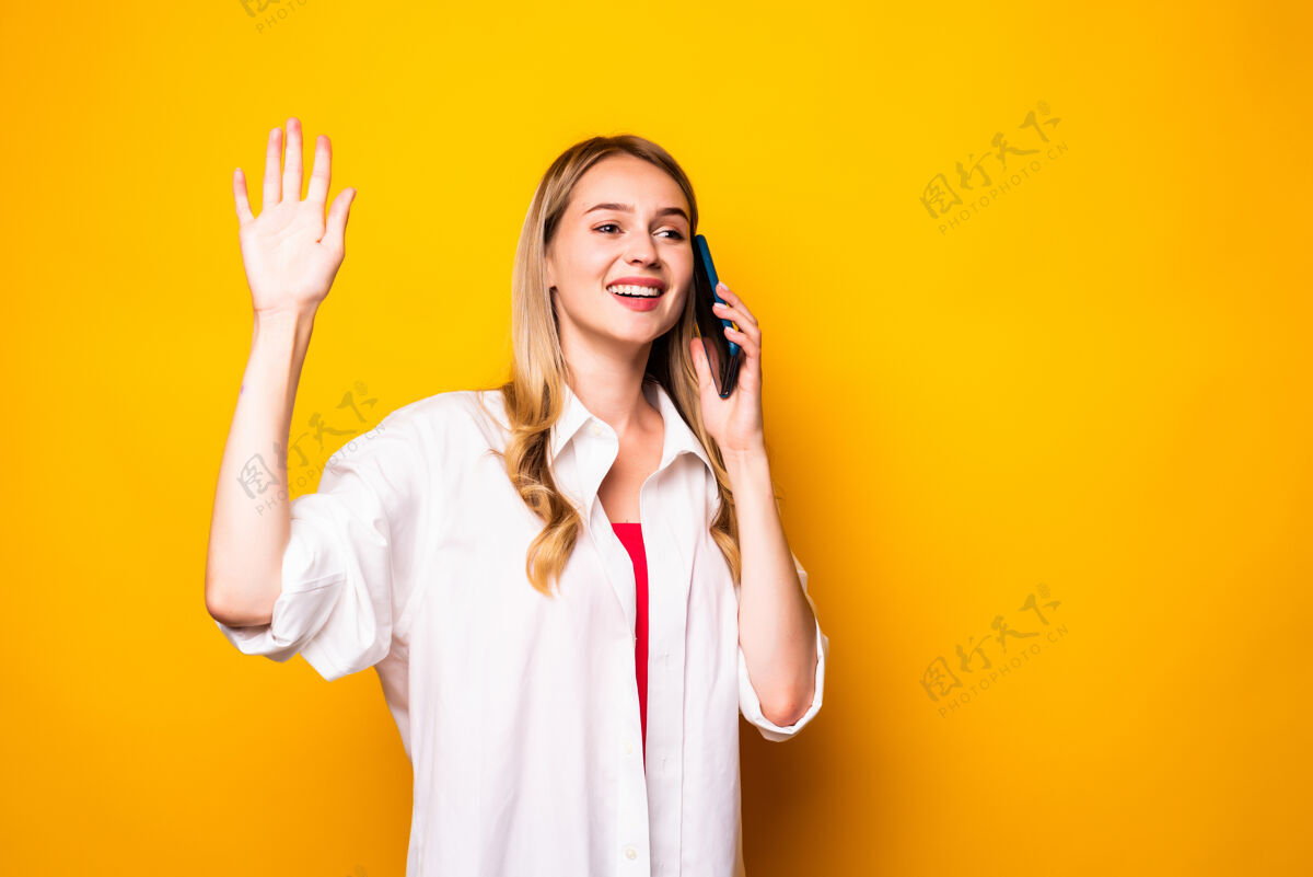 年轻年轻女子在黄墙上用智能手机挥手交谈可爱长移动