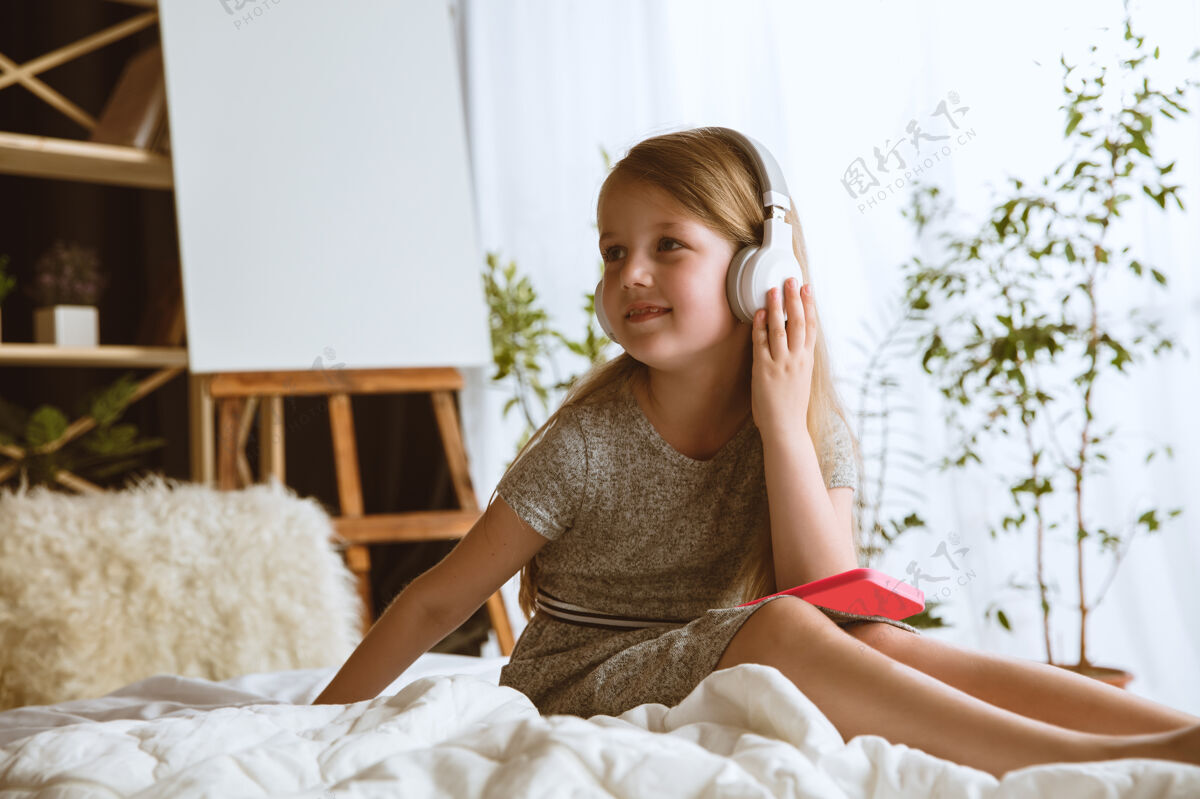 持有小女孩带着大耳机坐在床上听最喜欢的音乐 尽情享受耳机人脸