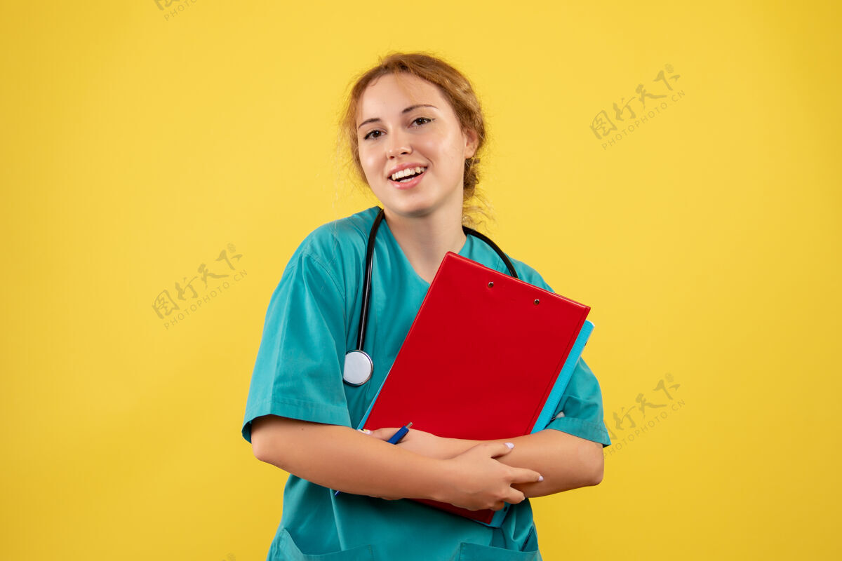 健康黄色墙壁上穿着医疗服的女医生带着论文和分析的正视图人漂亮快乐