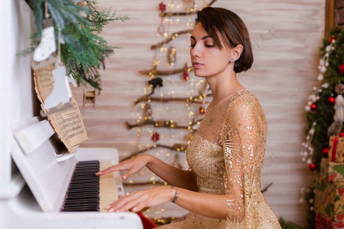 漂亮穿着金色圣诞晚礼服在家弹钢琴的女人房子键盘乐器