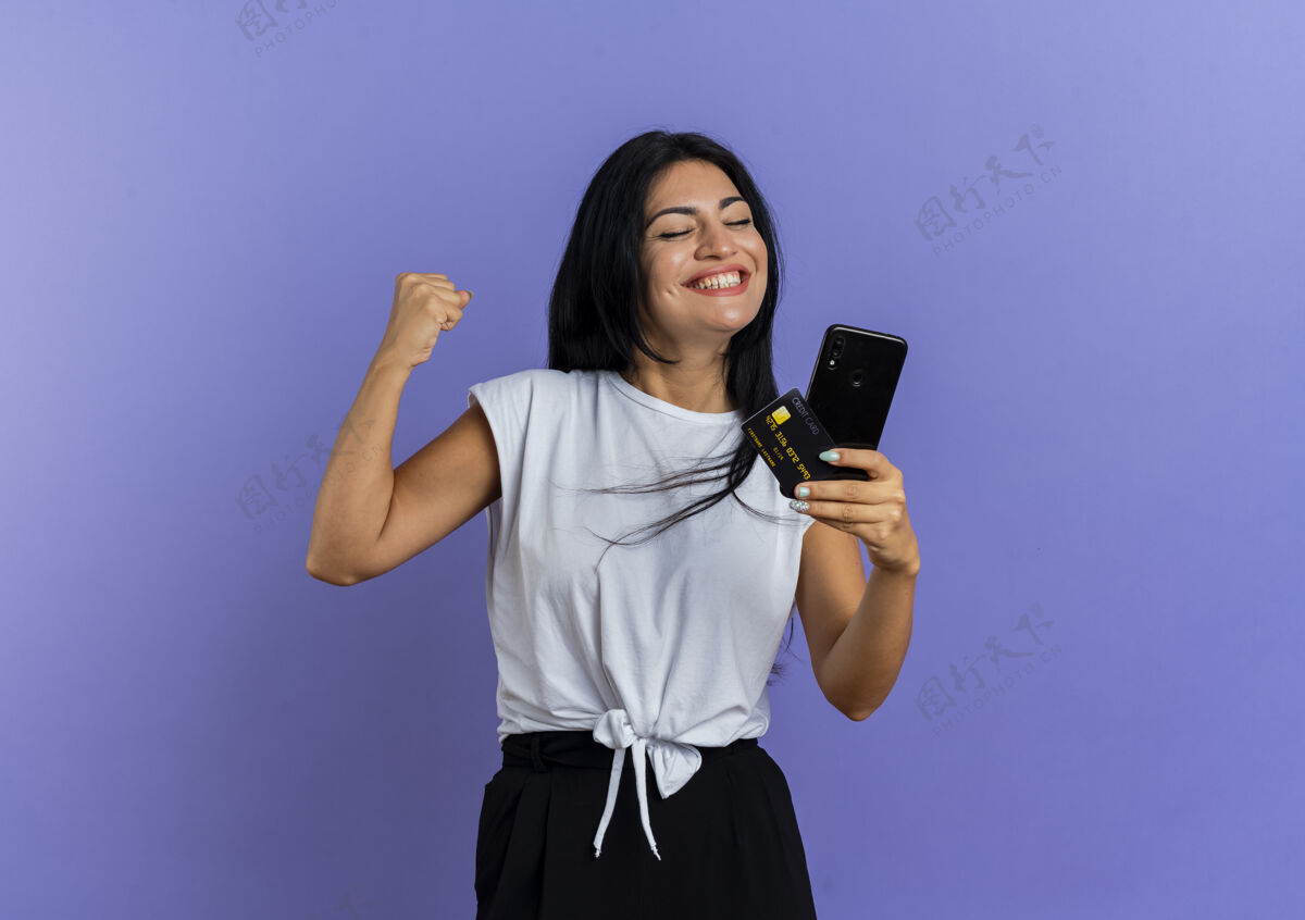 拳头微笑的年轻白人女孩握紧拳头 拿着电话信用卡复制空间电话