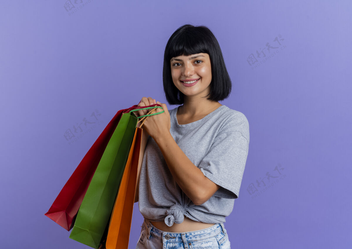 五彩微笑的年轻黑发白人女孩拿着五颜六色的购物袋紫色购物女孩