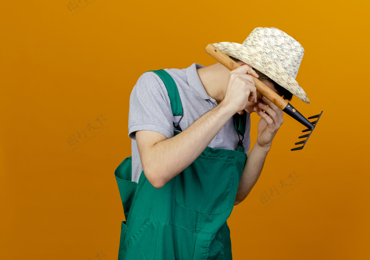 花园失望的年轻男园丁戴着园艺帽把手放在脸上 拿着耙子脸年轻失望