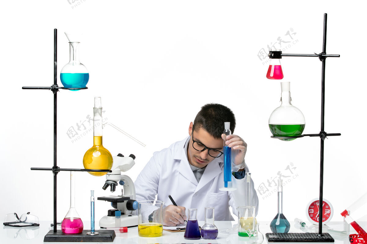 解决方案正面图身着医疗服的男性化学家坐在白色办公桌上拿着解决方案病毒-飞溅疾病科学喷溅病毒罐子