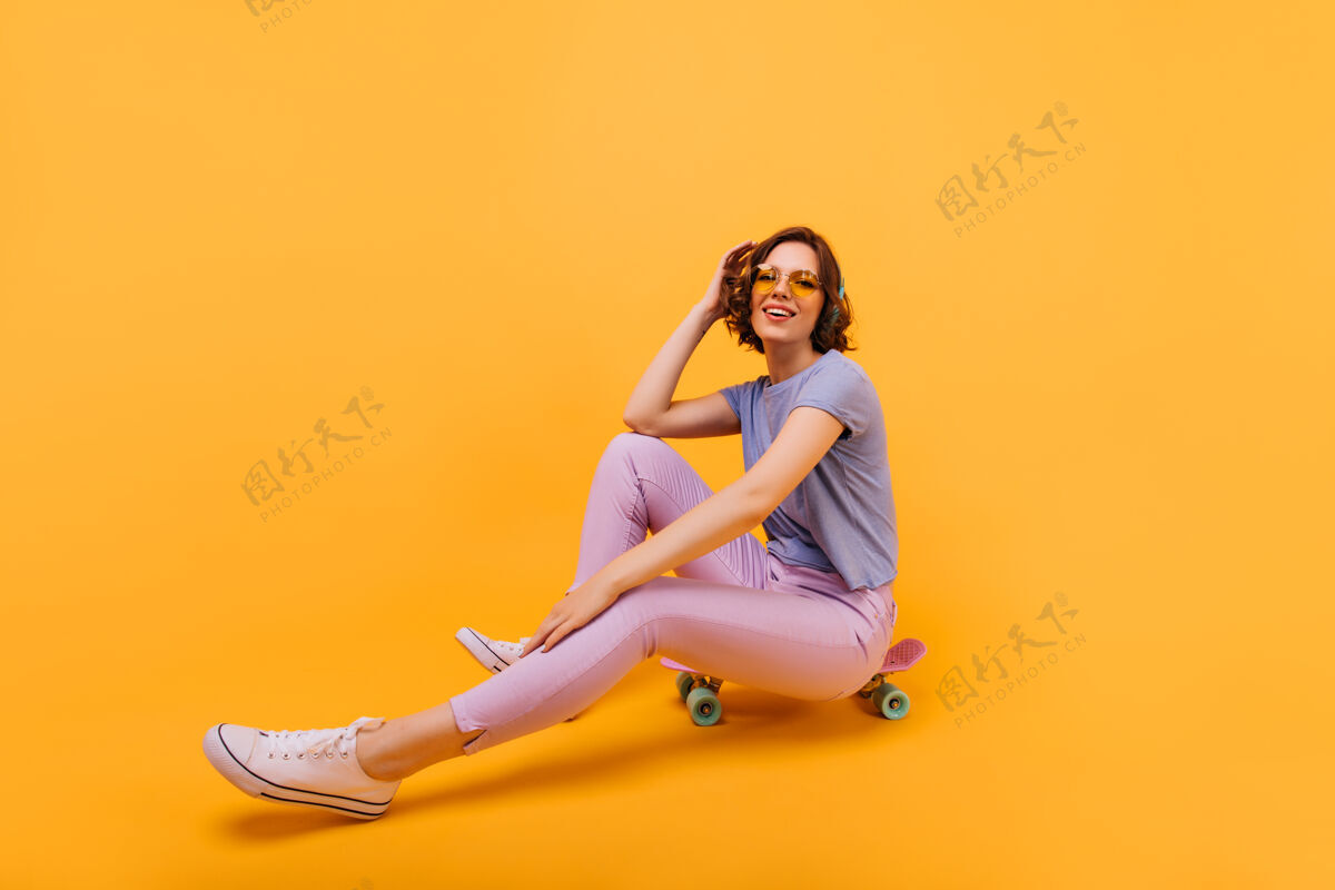 肖像穿着粉色裤子的欣喜若狂的女孩用长板表达美好的情感漂亮的女模特在滑板上摆姿势的室内照片模特无忧无虑玩