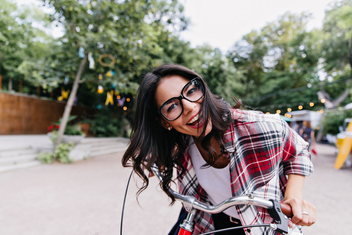 时尚兴奋迷人的女人骑在公园里户外照片笑着戴眼镜的黑发女孩在自行车上摆姿势自然乐趣肖像城市