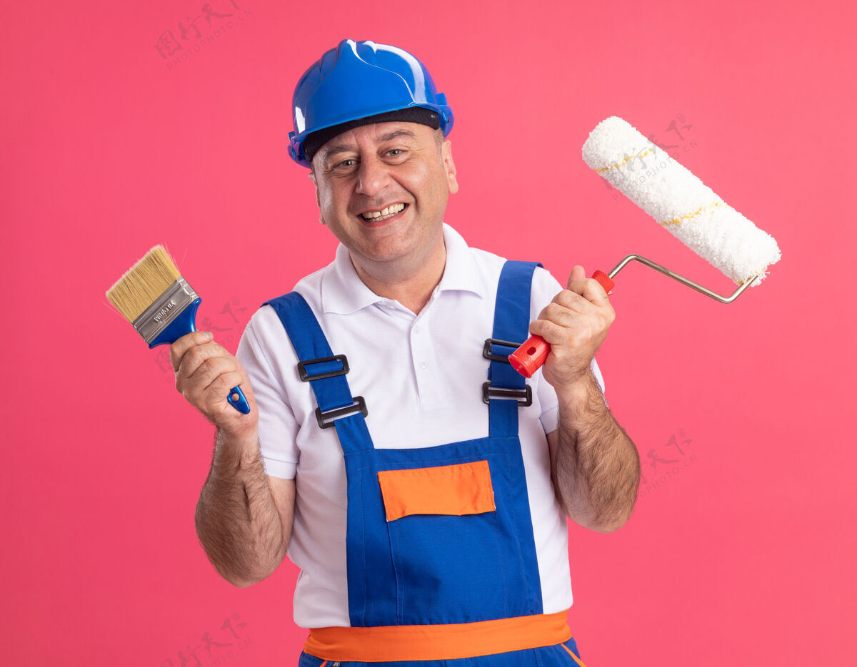 成年人微笑的成年白人建筑工人穿着制服拿着粉刷和滚筒刷男人刷子建筑工人