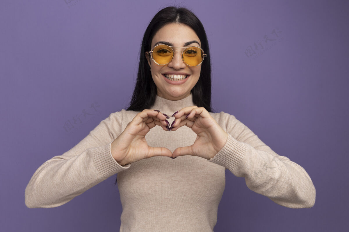 心微笑着漂亮的黑发高加索女孩在太阳眼镜手势心脏手上的紫色标志漂亮眼镜成人