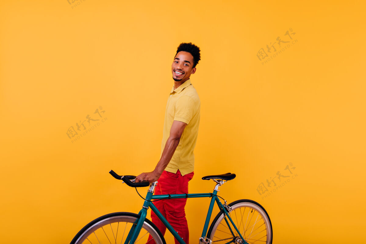 笑热情的黑人男子带着欢快的笑容和自行车合影室内照片是快乐的非洲男模和自行车站在一起表情微笑卷发