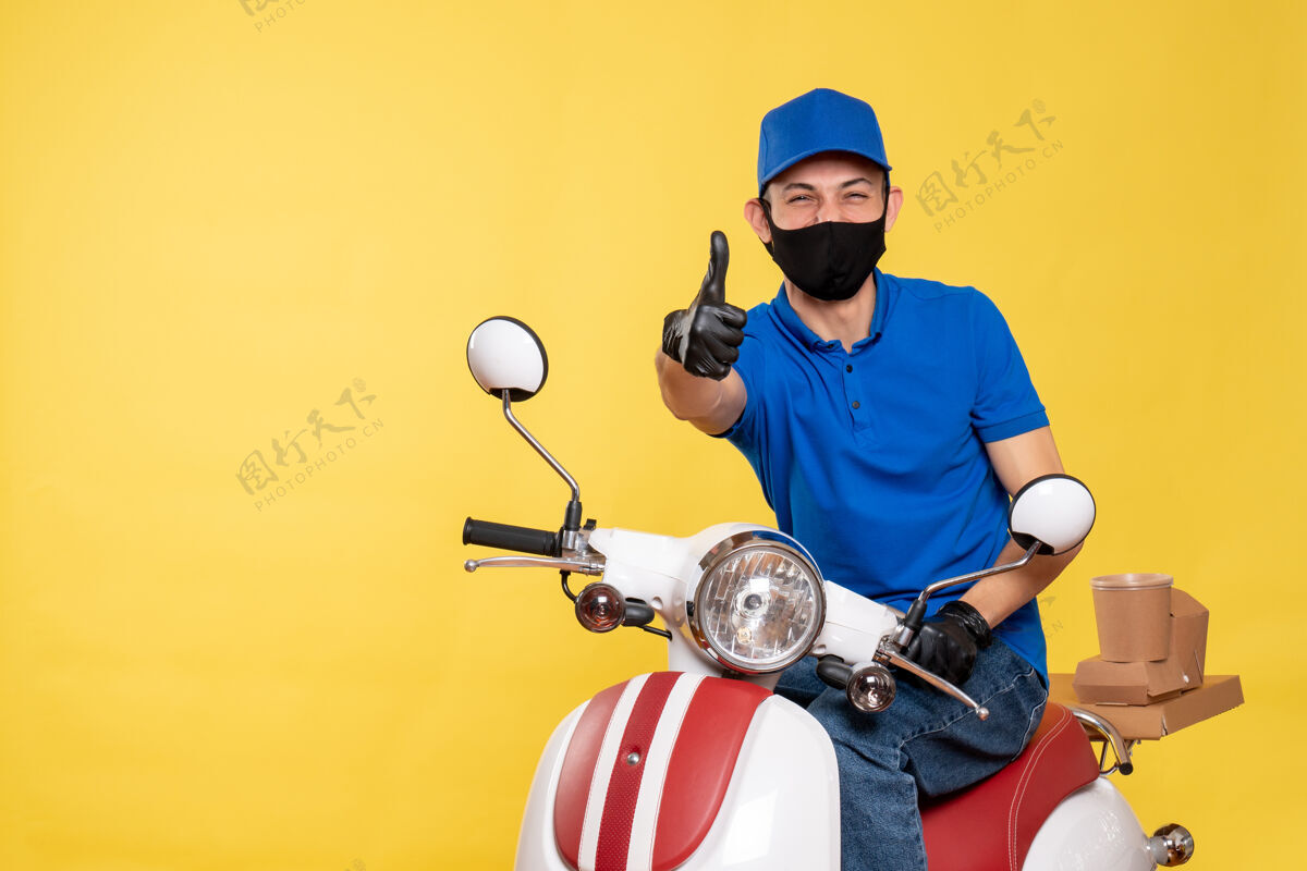 男性正面图身穿蓝色制服 戴着黄色口罩的男性快递员在工作自行车上笑着covid-大流行病毒服务工作车辆制服人