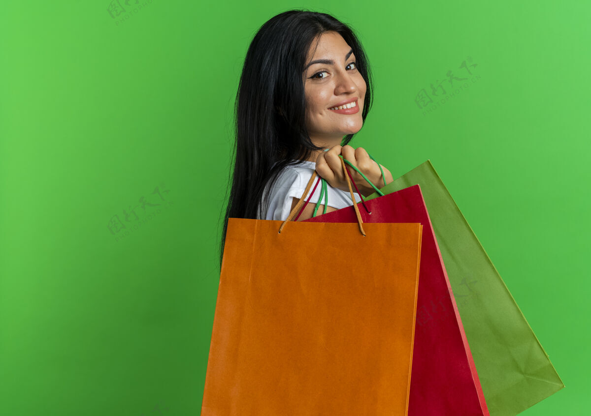 微笑微笑着的年轻白人妇女站在一边拿着纸购物袋隔离在绿色背景与复制空间女人购物纸