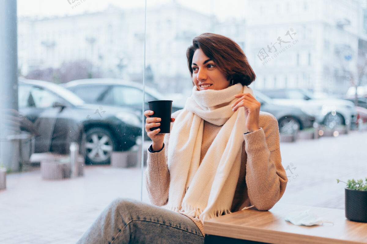 冷一个女孩在舒适的咖啡馆里用一杯热咖啡取暖微笑窗户咖啡馆