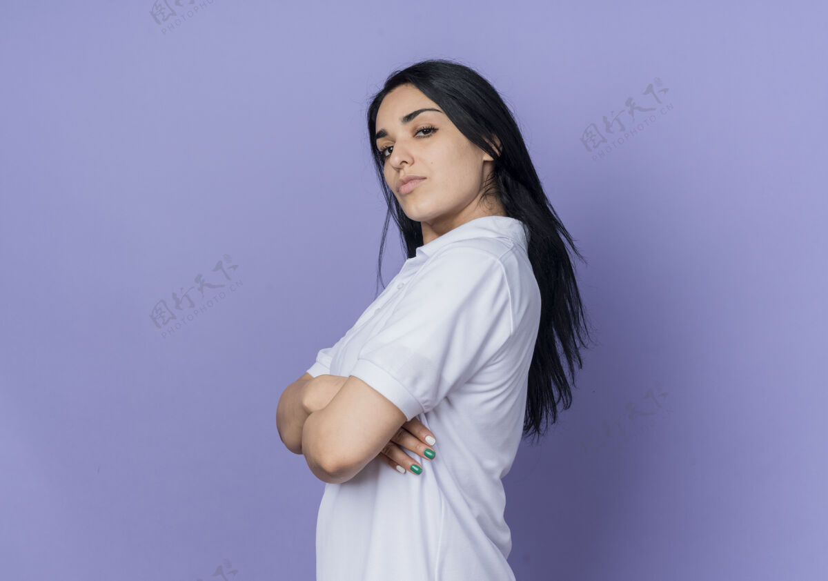 黑发自信的年轻黑发白种人女孩站在紫色的墙上女人侧身年轻