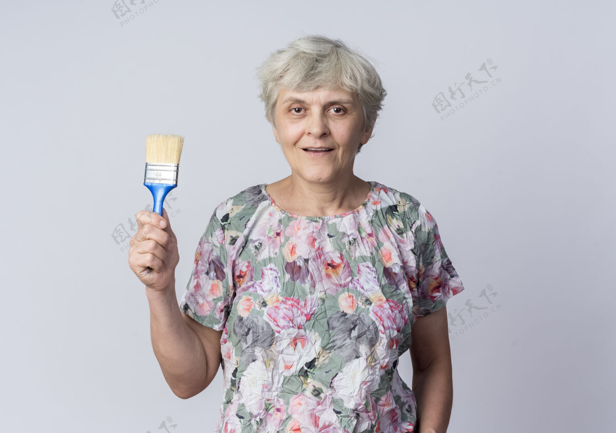 请拿着高兴的老妇人把油漆刷孤立在白墙上刷子老人女人