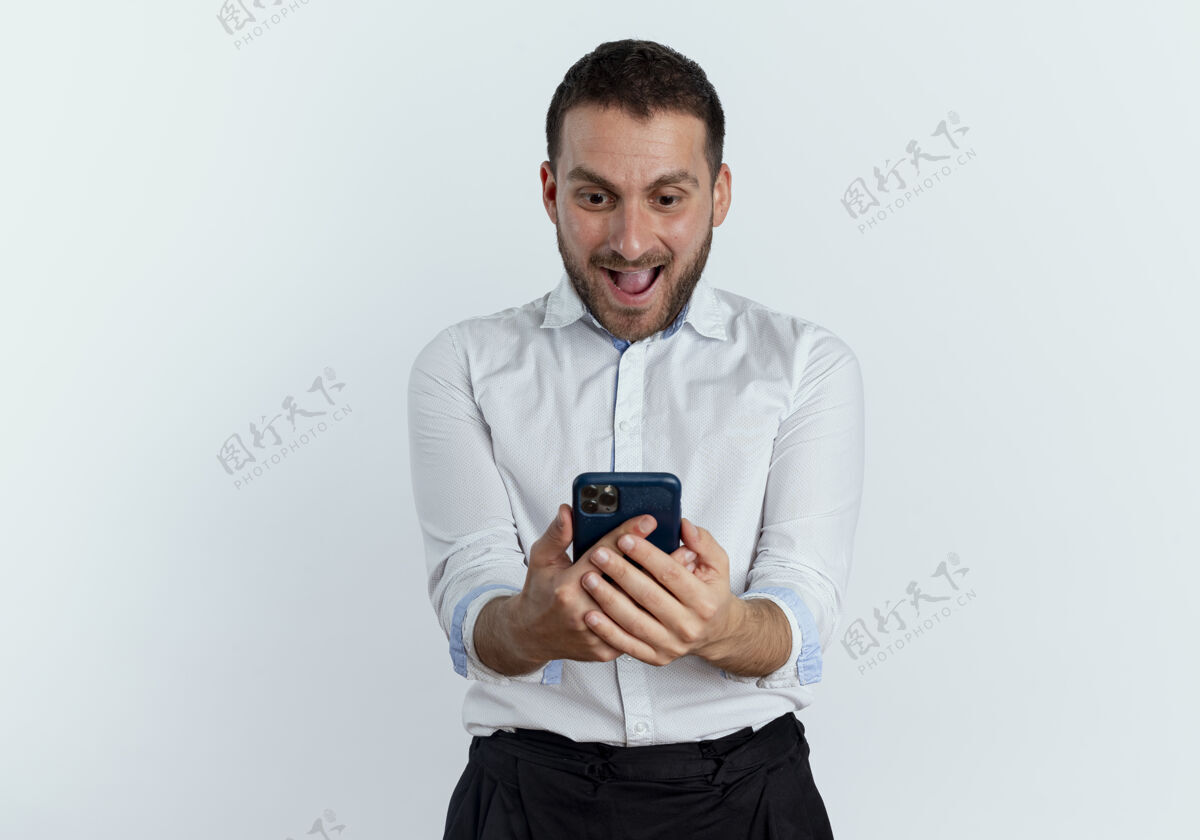 帅气兴奋的帅哥拿着手机 看着隔离在白墙上的手机商人优雅衬衫