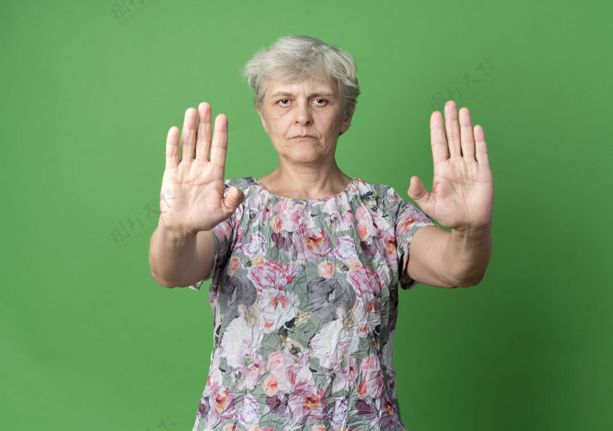 二自信的老妇人用两只手在绿色的墙上做手势停止手势自信手势绿