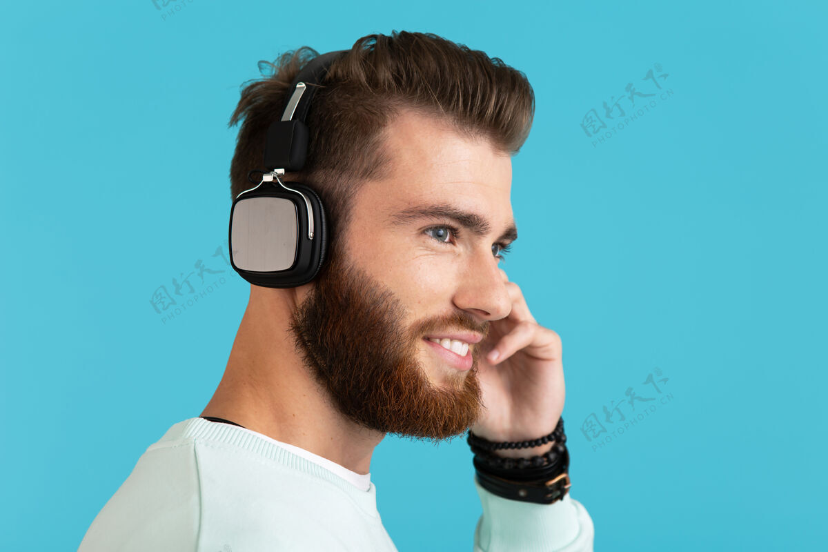 音频时尚迷人的年轻胡须男子的肖像在无线耳机上听音乐现代风格自信的情绪在蓝色背景上孤立城市家伙享受