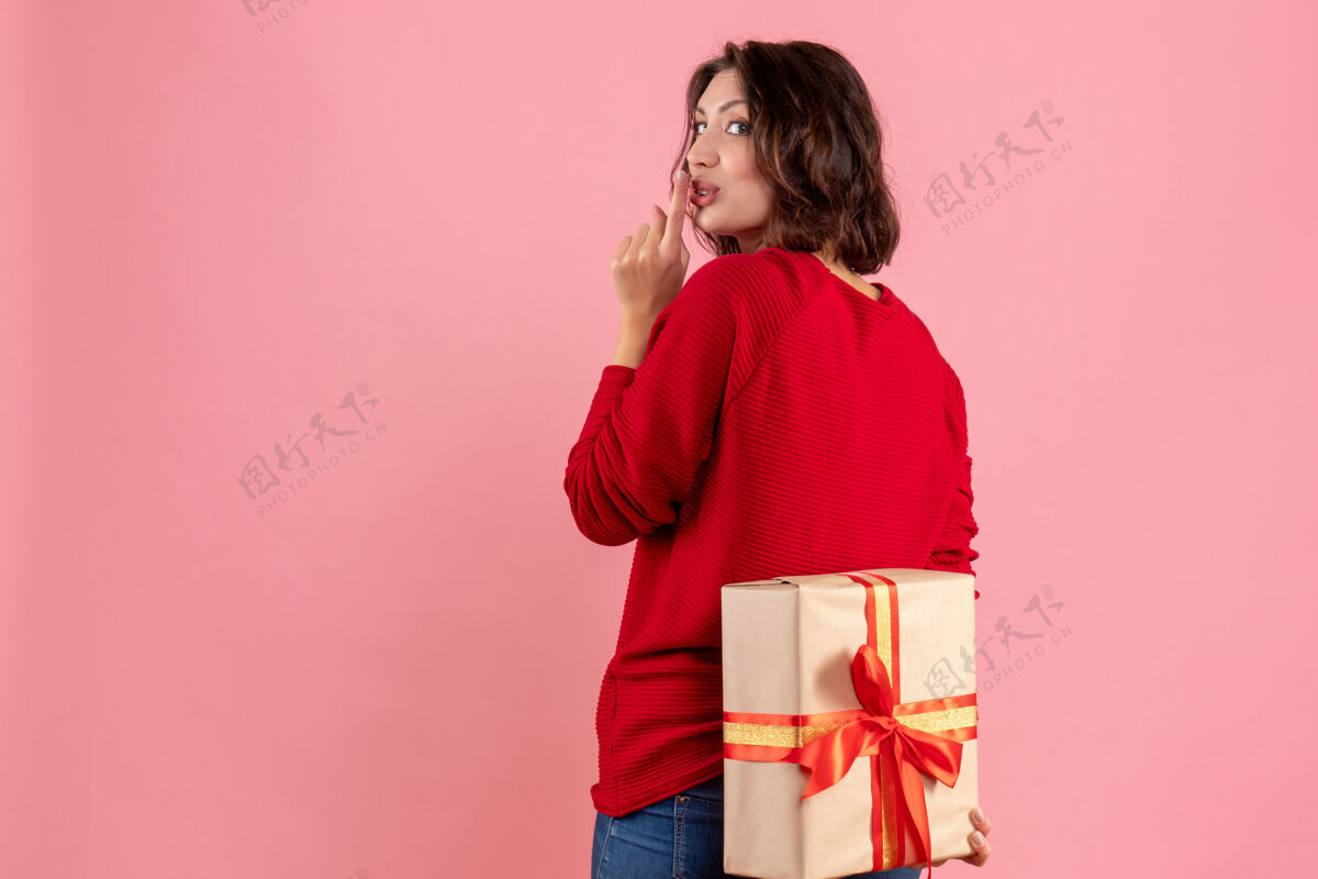 女人前视图年轻女性隐藏圣诞节礼物背后的粉红色节日圣诞节粉红