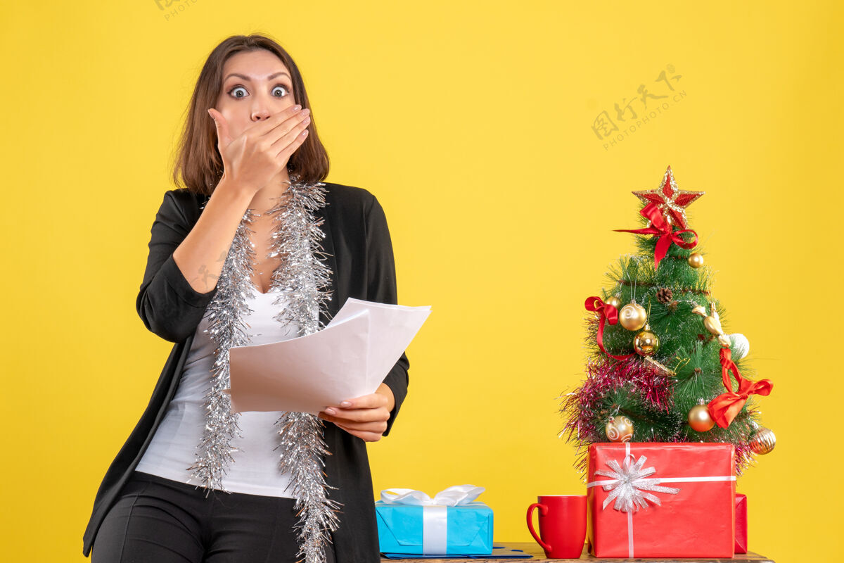 黄色圣诞气氛与惊喜美丽的女士站在办公室里 拿着文件在黄色的办公室快乐肖像模特
