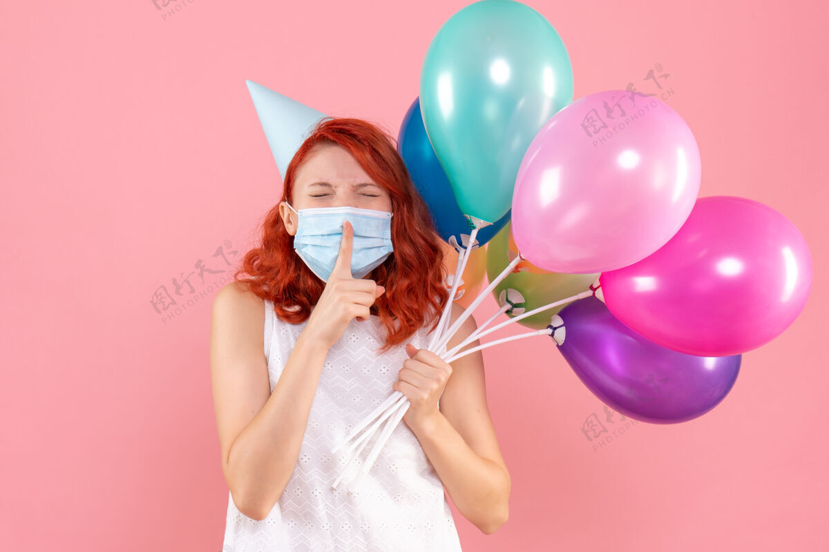 快乐正面图年轻的女性手持彩色气球在面具上浅粉色举行年轻女性病毒