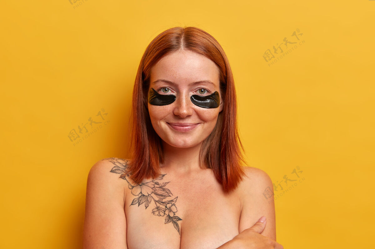 清洁隔离镜头美丽的红发女性穿着黑色胶原蛋白贴皱纹和皮肤干燥 在美容院接受美容程序 光着肩膀 隔离在黄色的墙壁下巴清新治疗