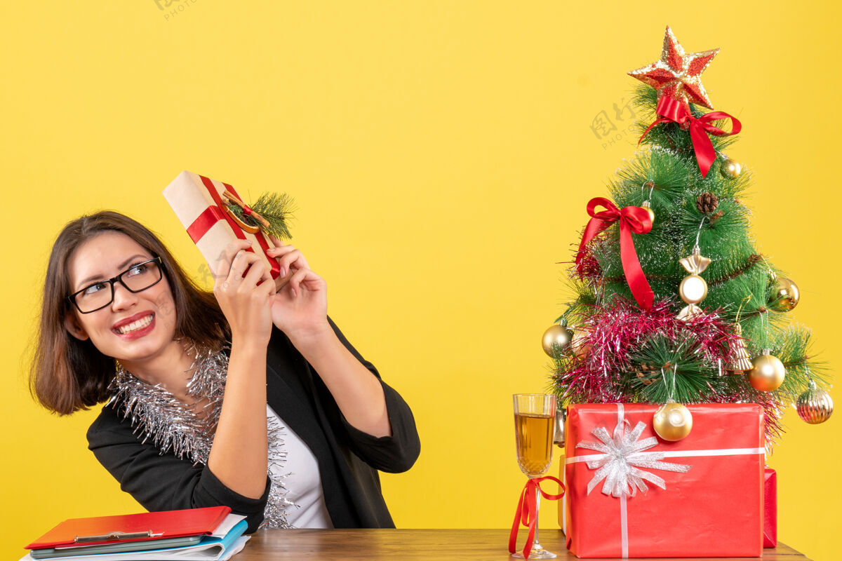 庆典一位穿着西装 戴着眼镜 拿着礼物 坐在办公室里一棵圣诞树旁的商务女士吓了一跳时尚漂亮眼镜