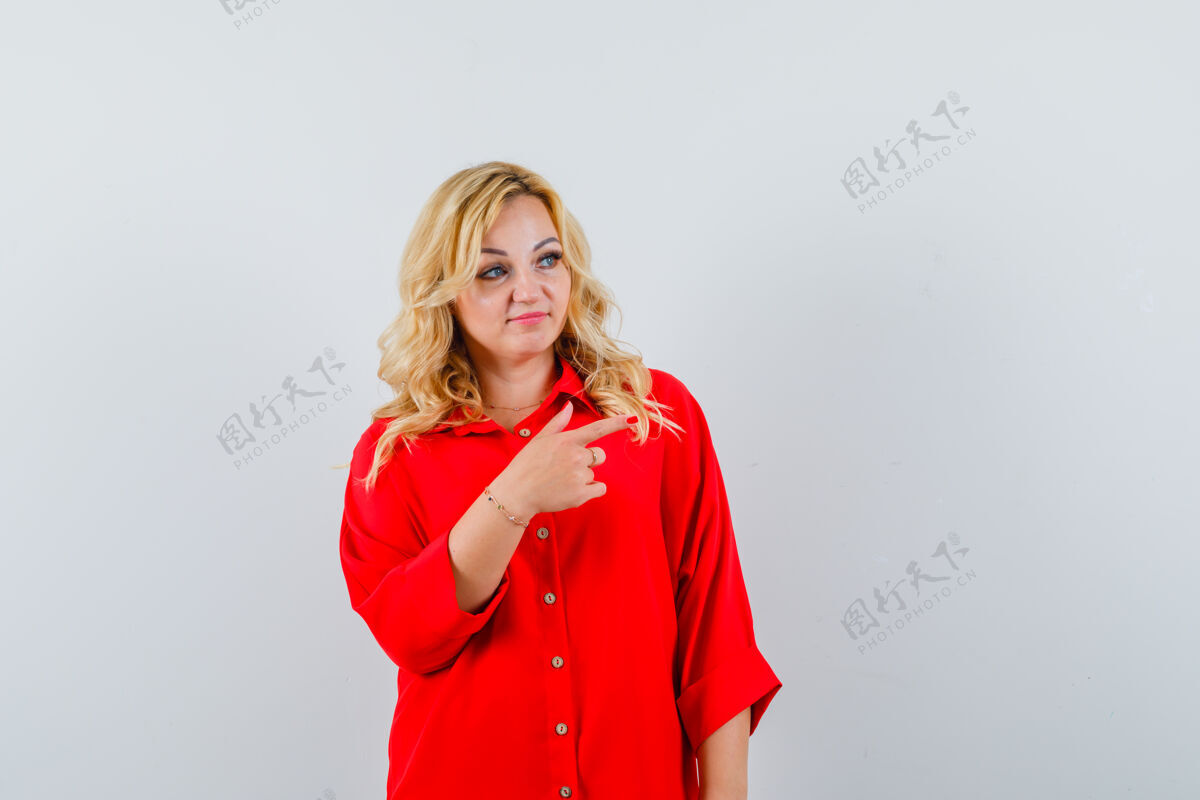 目录一个金发女人用食指指着右边 穿着红色罩衫 看起来很漂亮 正视图皮肤护理头发微笑