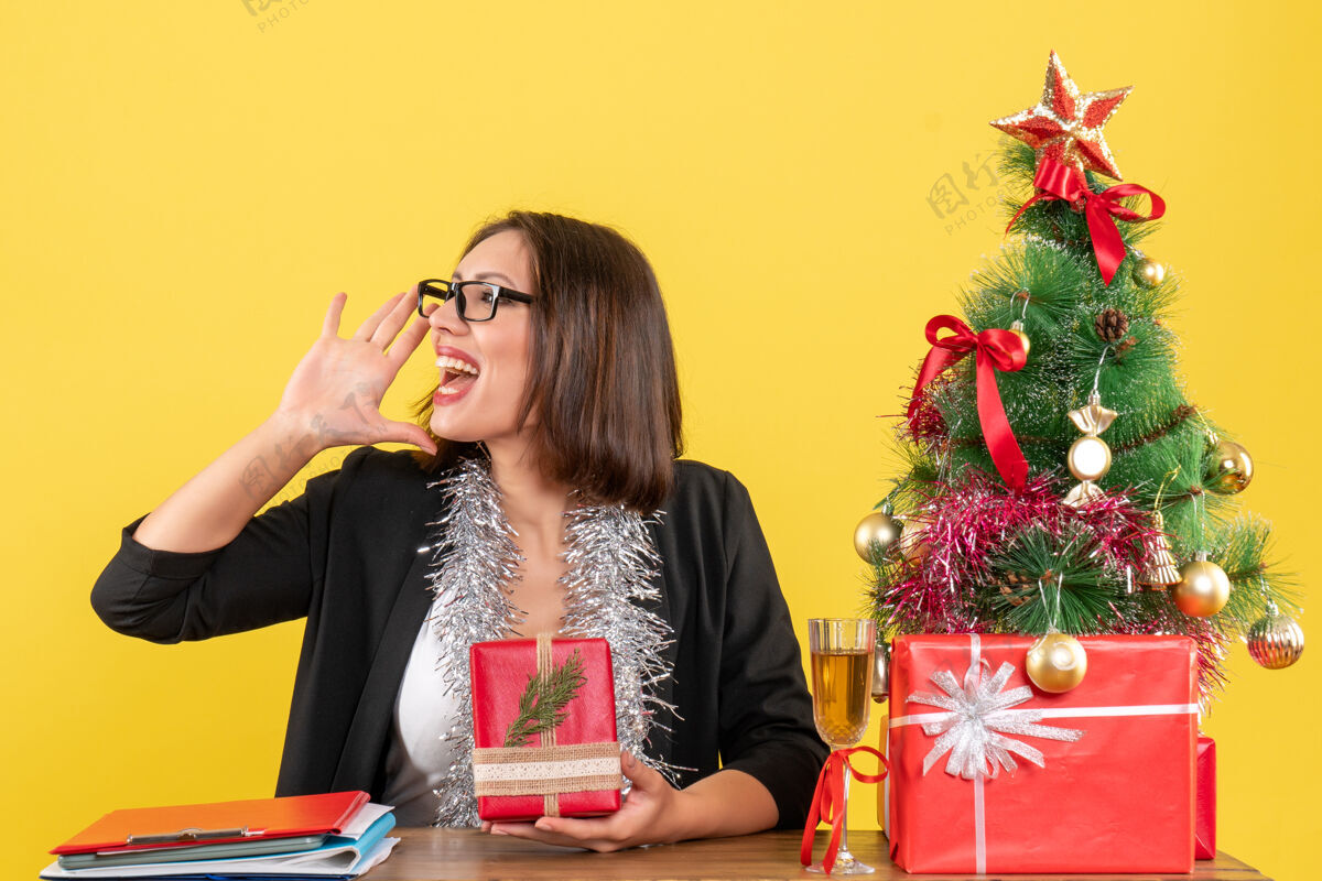 电话一位穿着西装 戴着眼镜 展示礼物的商务女士在办公室里给别人打电话 坐在一张桌子旁 桌上放着一棵圣诞树女士套装快乐