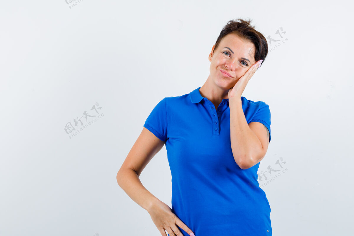 人成熟的女人 穿着蓝色t恤 面颊靠在手掌上 面带沉思 俯视前方新鲜健康微笑