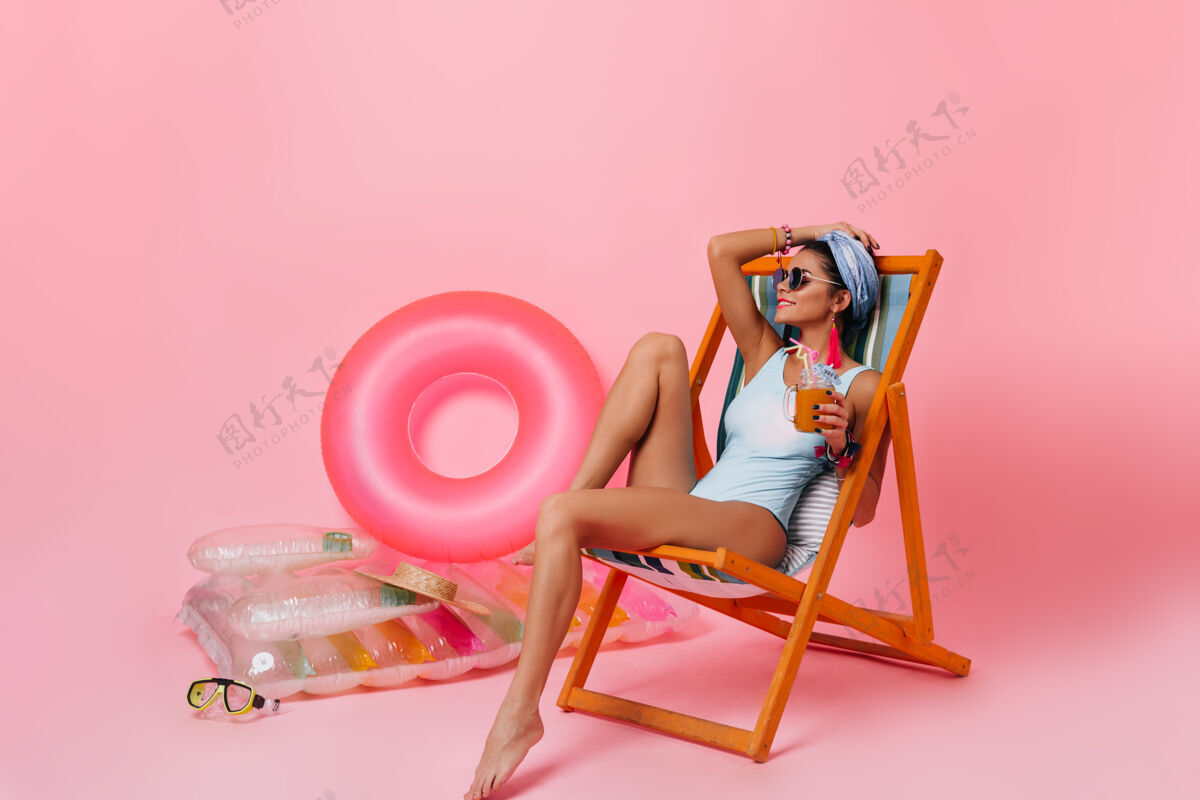 快乐迷人的黑发女人在躺椅上喝果汁微笑年轻放松