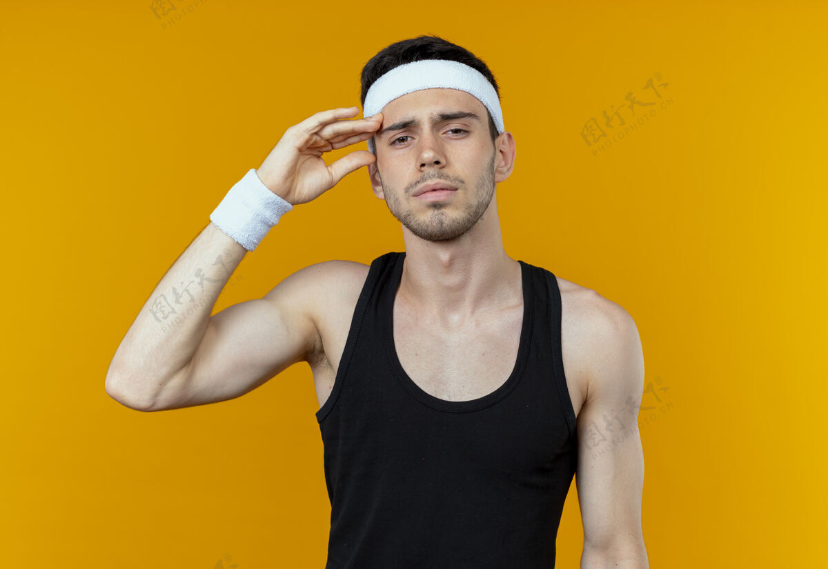 头部戴着头巾的年轻运动型男子站在橙色背景下 看着相机抚摸着他的头 又累又无聊站立疲倦年轻