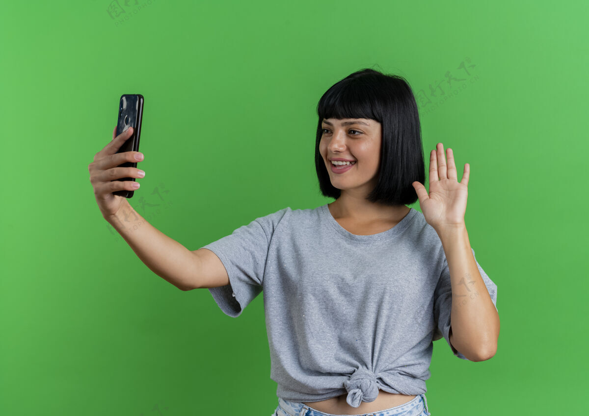 空间年轻的黑发白人女孩微笑着举手 看着绿色背景上的手机和复印空间女孩手电话