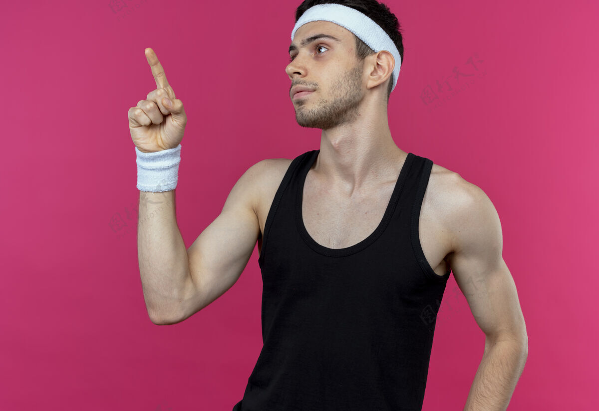 表情戴着头巾的年轻运动型男子站在粉色背景上 一边看着一边 一边用手指着一边 表情自信侧身站立年轻